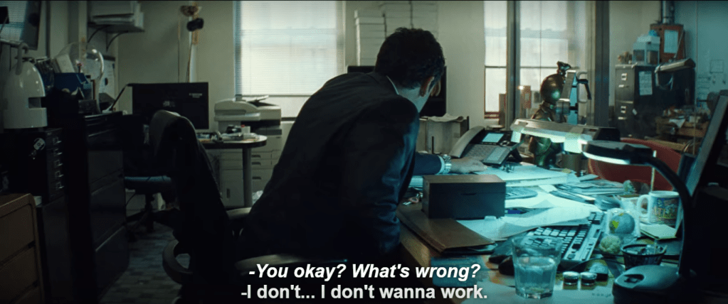 A view of Ratner's cluttered and cramped back office. All surfaces are full of various items. Howard is centered, seated at his desk and leaning toward an office phone. Subtitle: (italics) "-You okay? What's wrong?" (non-italicized) "-I don't...I don't wanna work."