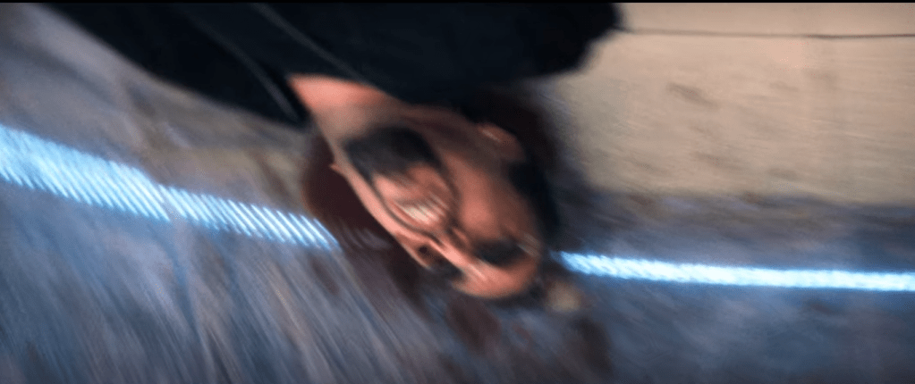 A closer shot of Ratner's body, upside down in the ceiling reflection, head centered with blue line passing through and more blood visible in a shape suggestive of a halo The image has been blurred, giving it more of an appearance of 2-dimensionality.